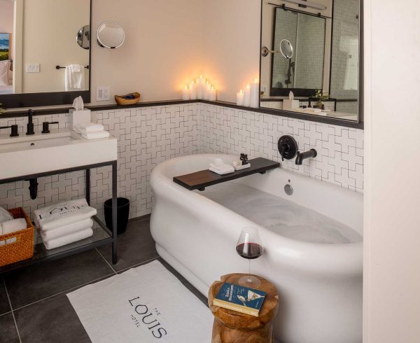 Photo of a guest bathroom at The Louis Hotel with a drawn bubble bath and glass of wine next to the tub.